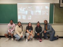 five students kneel posed in front of blackboard